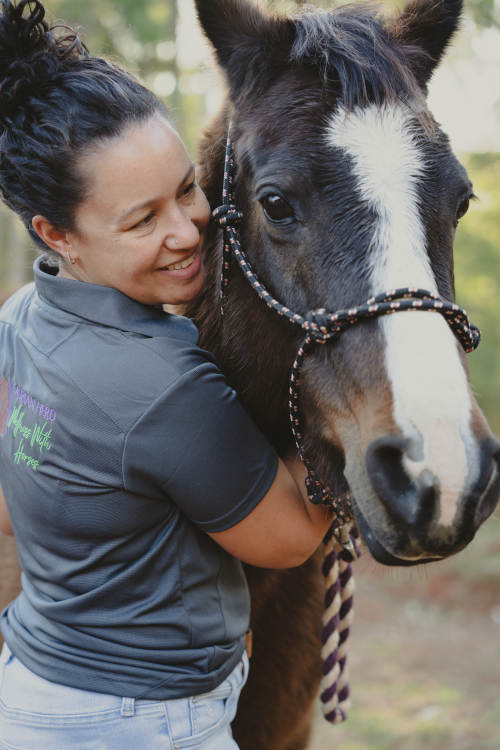 Equine facilitated learning practitioner, Camille hugging a brown horse at Boyland Queensland